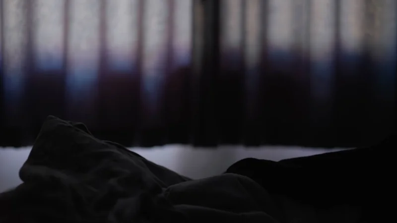 A figure asleep under blankets in low blue light.